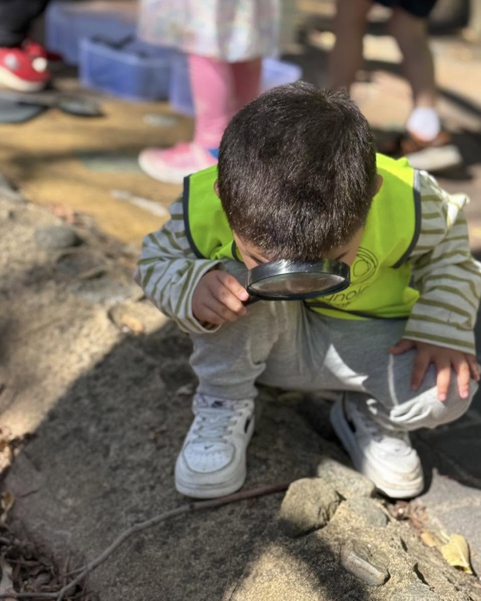 Child using a magnifying glass to explore the sandpit